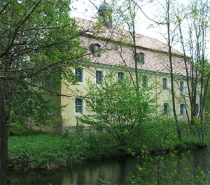 Grüne Bäume verstecken die Barockfassade des Neuhausener Schlosses, das von zwei Seiten mit Wasser umgeben ist. Über den Sanierungsstand Außen und Innen kann man sich am kommenden Sonnabend informieren