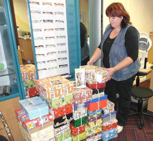 Die Augenoptikerin Heike Woucznack stapelt 32 Kartons der Aktion „Weihnachten im Schuhkarton“ in ihrem Geschäft. Alle stammen von einer einzigen Spenderin