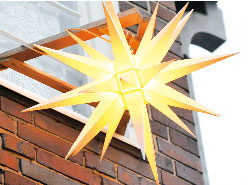 Der Herrnhuter Stern leuchtet im warmen Gelb vom Gemeindehaus in die Hans-Sachs-Straße hinunter