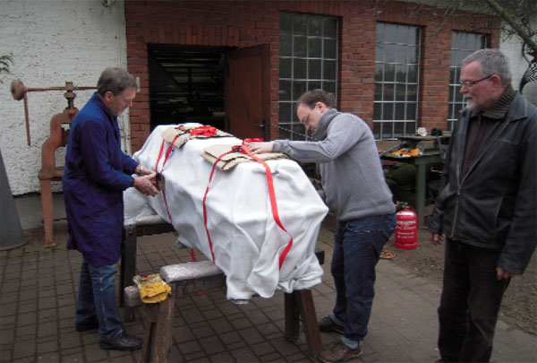 Angekommen in der Werkstatt des Kunstschmiedes Georg Ignaszewski (r.) lösen Andreas Hammer vom Kirchbauverein und der Diplom Restaurator Mario Jehle (v.l.) die Transportsicherungen. Wie Frank Henschel vom Kirchbauverein erklärt, ist der Sarg etwas heimlich aus Forst auf Reisen gegangen, um die Totenruhe nicht zu stören 	F: Kirchbauverein